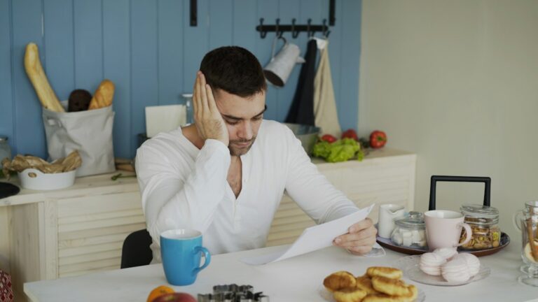 Person reviewing a health insurance statement, calculator, prescription bottles, and payment notes at a kitchen table